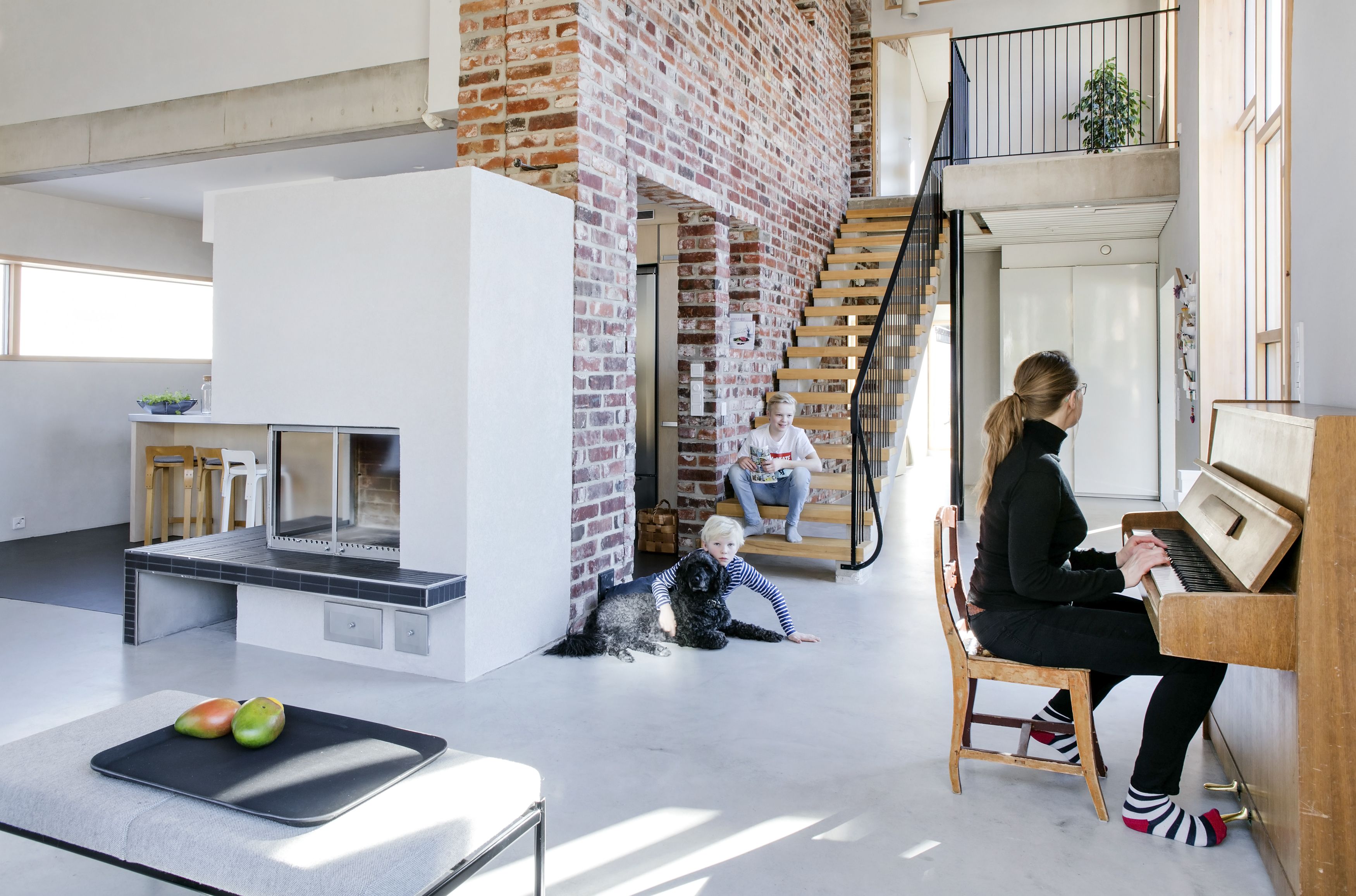 Porrasratkaisua mietittiin pitkään. Lopulta löytyi yksinkertainen malli, joka kelpasi kaikille. Itse tehdyn portaikon runkona on muottiin valettu ja raudoitettu betoni, askelmat ovat saarnipuuta. Ilmarin kainalossa Alex-koira, rapuilla Iisakki ja pianon ääressä Pirjo.