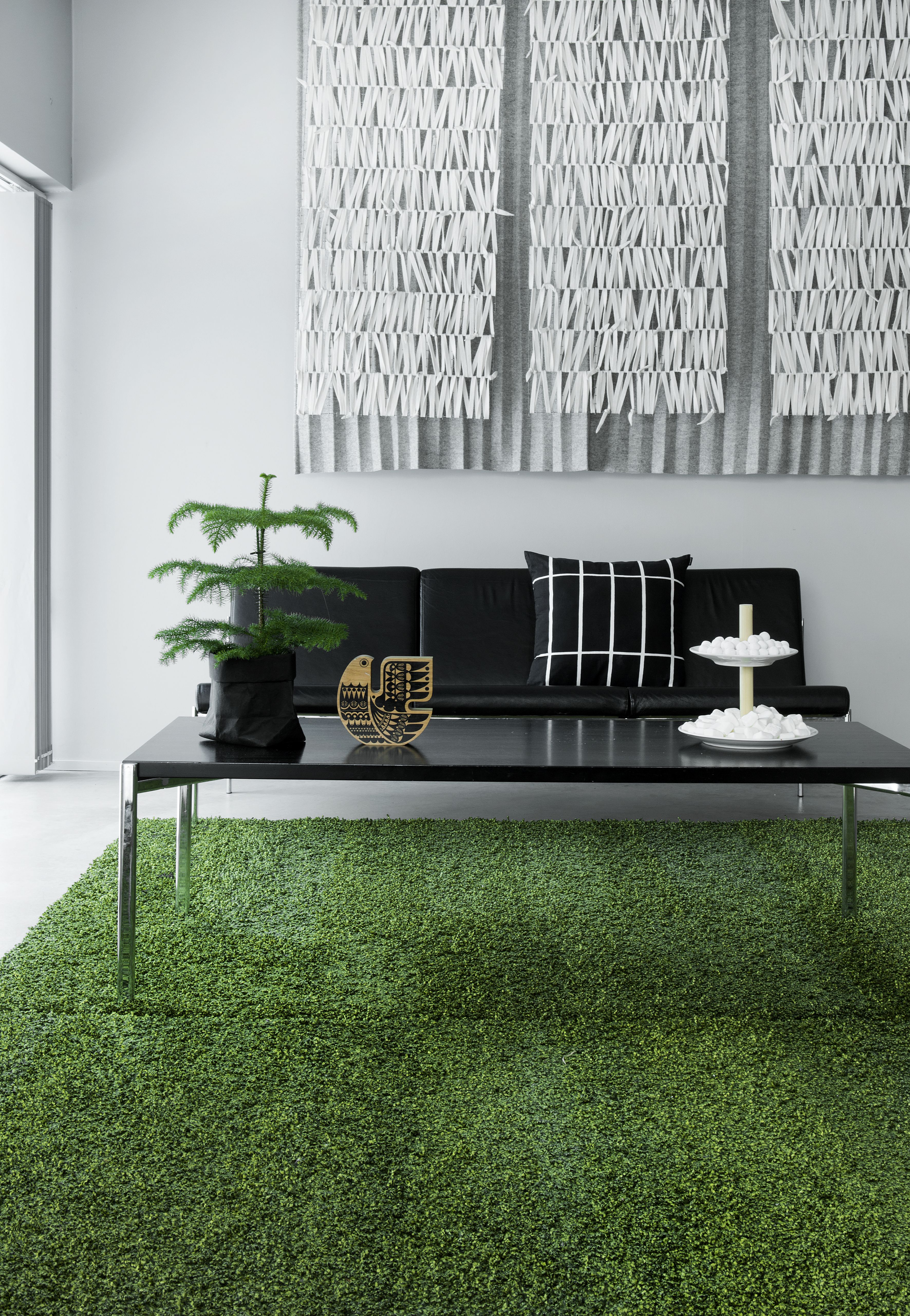 Olohuoneen lattialla on kaksi identtistä sammaleenvihreää mattoa, jotka hankitiin Sisustusliike Decorasta. Ilmari Tapiovaaran suunnittelema Kiki-sohva ja -sohvapöytä ovat Artekin. Pöydällä oleva Sielunlintu on Sanna Annukan. Sisustustyyny on Marimekon. Ääniä vaimentava huopataideteos Riimejä tilattiin tekstiilitaiteilija Eeva-Kaisa Timliniltä.