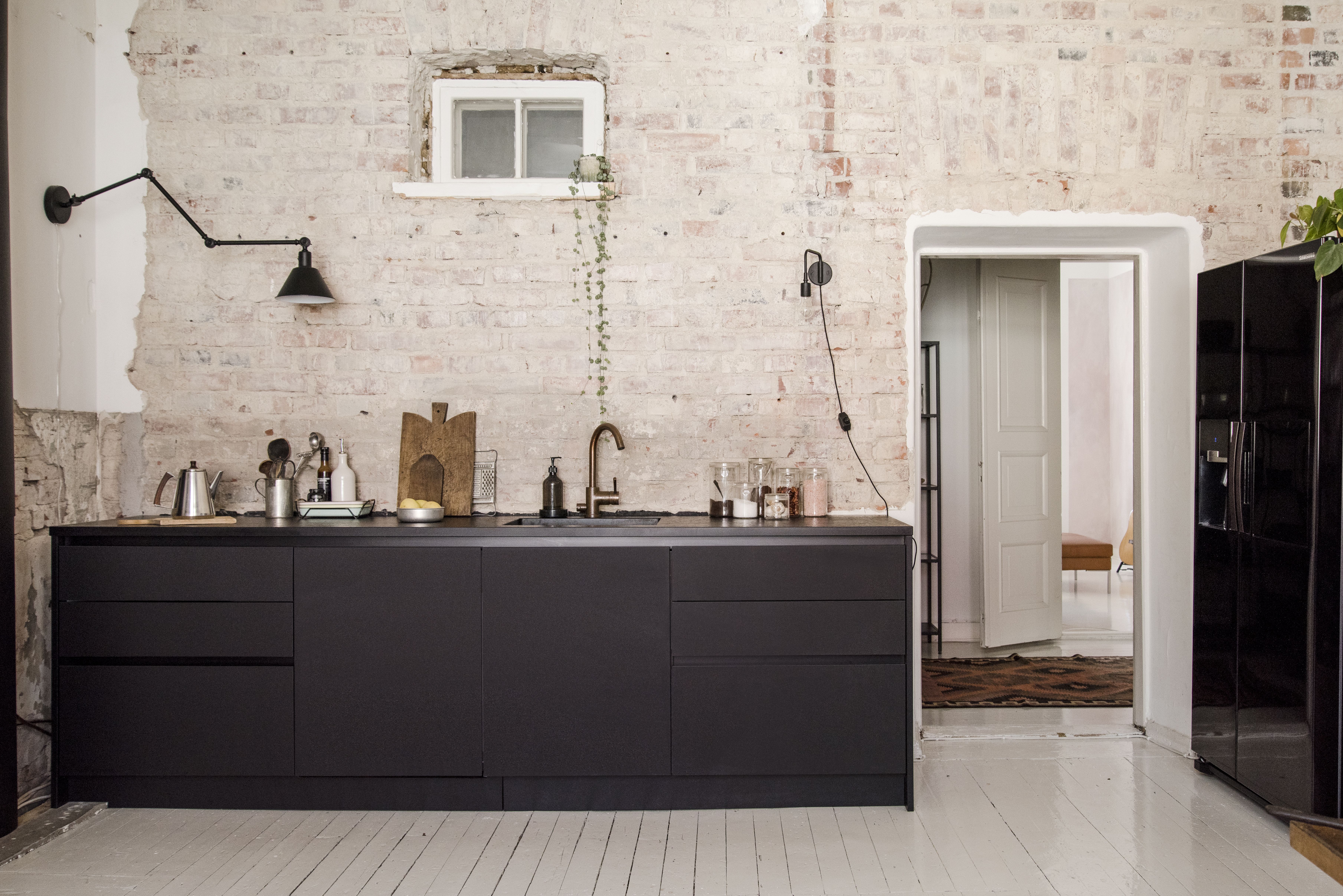 Yläkaapittoman mittatilauskeittiön toteutti Kitzen. Mattamustat ovet ovat Fenix-nanolaminaattia ja taso helppohoitoista kvartsikomposiittia, joka leikattiin käsin myötäilemään epätasaisen seinän muotoja. Tapwellin kuparinen hana patinoituu kauniisti ajan myötä. Takaseinä kaivettiin tiilelle, harjattiin pölystä ja käsiteltiin venelakalla.