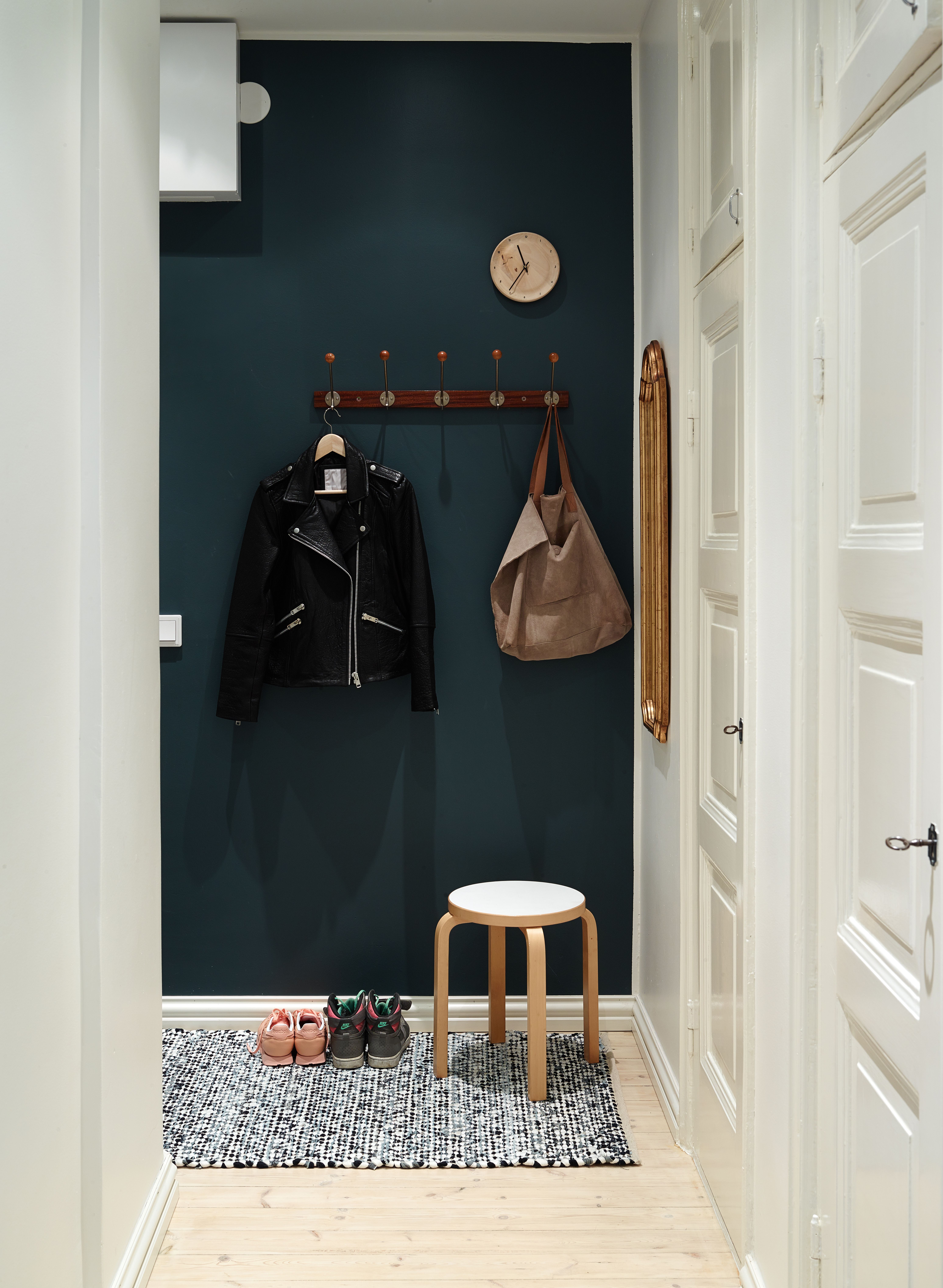 Eteisen seinään valittiin tehosteväriksi Tikkurilan Petrooli-sävy. Naulakko, seinäkello, peili ja Artekin E60-jakkara riittävät tilan kalusteiksi. Vanhat, kauniit kaapinovet kunnostettiin remontissa.